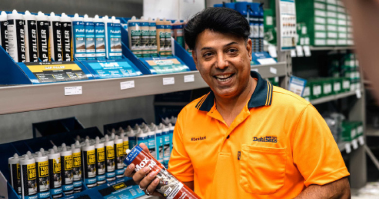 Dahlsens team member smiling at the camera holding Floor adhesive products.