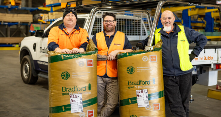 Three men in a warehouse, smiling to camera